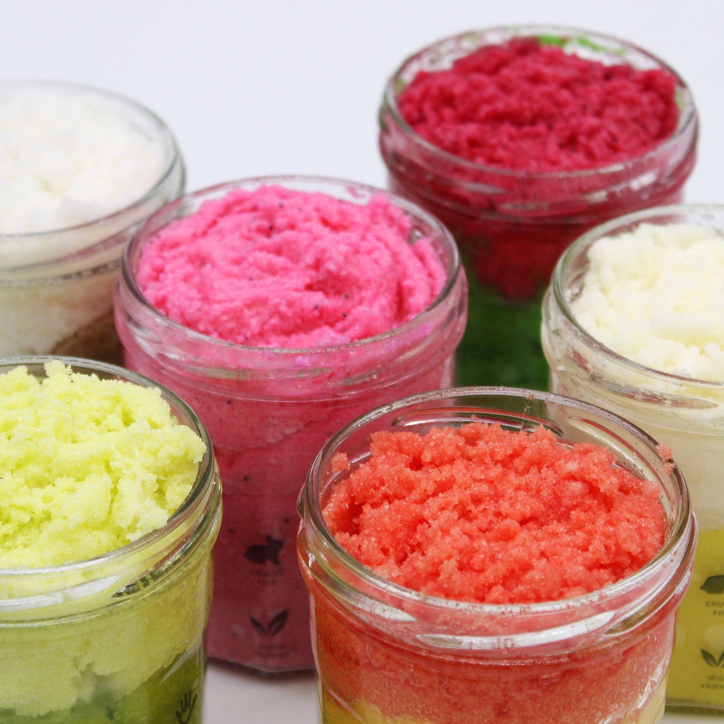 Tarros de cristal con exfoliante de azúcar en colores vibrantes, texturas granulares y aromas frutales.