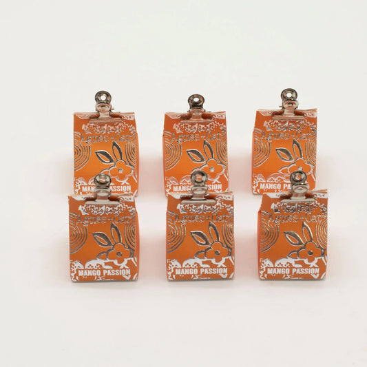 Seis bálsamos labiales naranja de Agnes + Cat con diseño floral plateado y pinza metálica superior sobre fondo blanco.