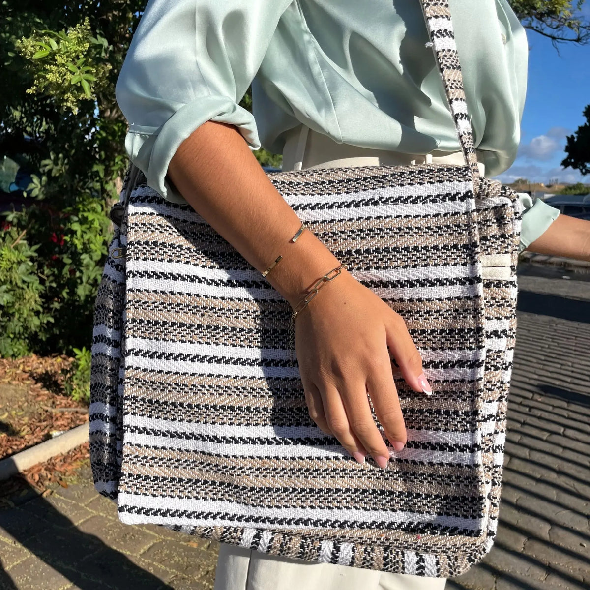 Bolso para portátil rectangular, tejido con rayas horizontales en tonos crema, gris y negro, con correa larga al hombro.