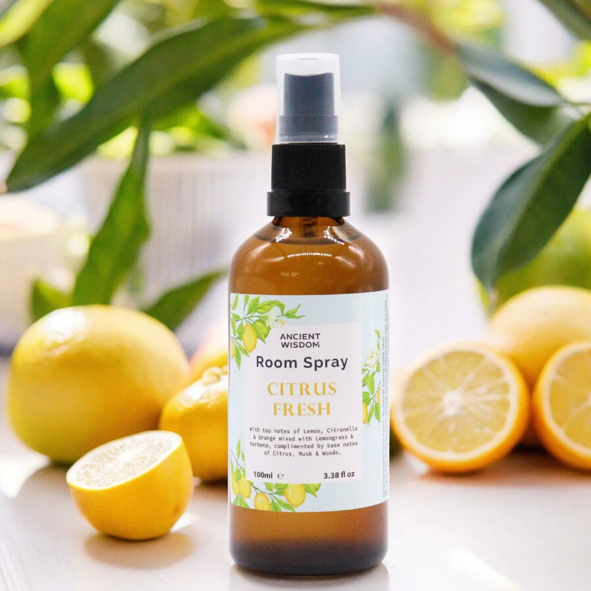 Spray de hogar en frasco ámbar de 100ml con atomizador negro, rodeado de limones frescos sobre fondo desenfocado.