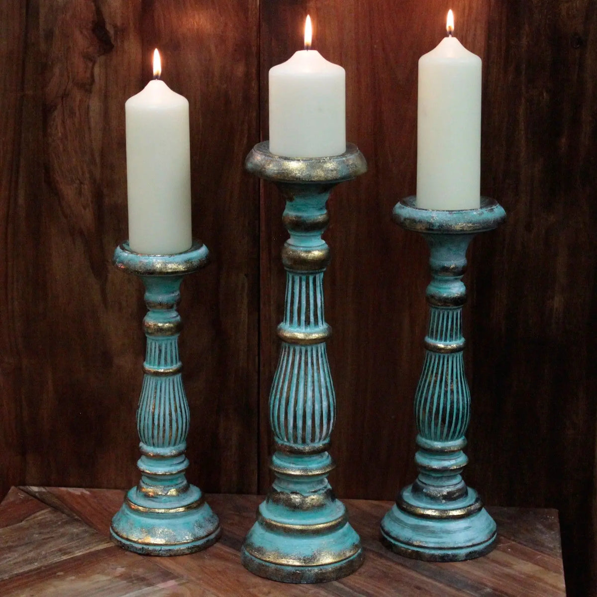 Tres candelabros de madera vintage con acabado turquesa y dorado, sosteniendo velas blancas encendidas.