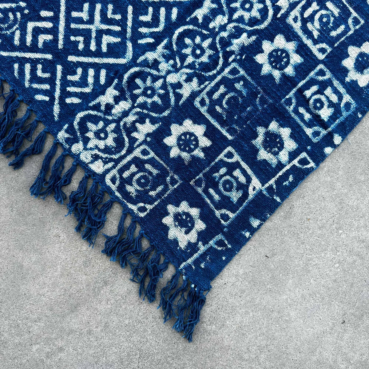 Alfombra azul con estampado floral en blanco, hecha de algodón, estilo bohemio, con flecos decorativos.