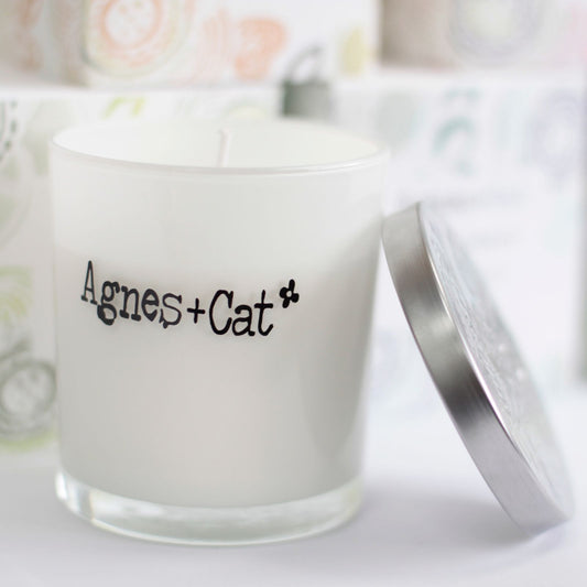 Vela aromática blanca en vaso de vidrio con tapa plateada, estilo moderno y elegante, de Agnes + Cat.