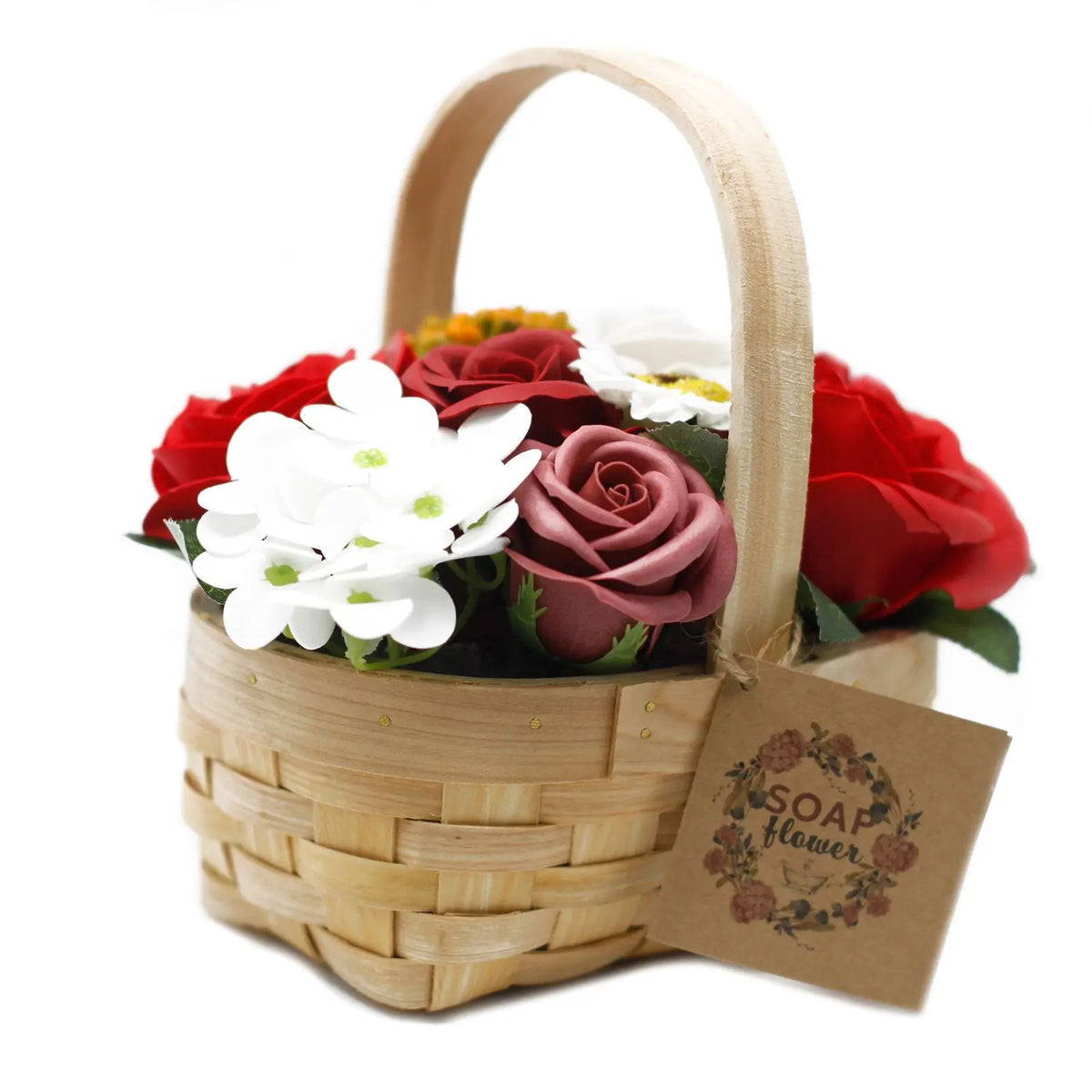Canasta de mimbre con rosas de jabón rojas y flores blancas decorativas, con etiqueta colgante, sobre fondo blanco.