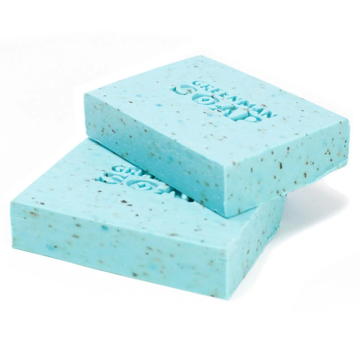 Dos pastillas de jabón azul claro, con motas oscuras y grabado "Greenman Soap" sobre fondo blanco.