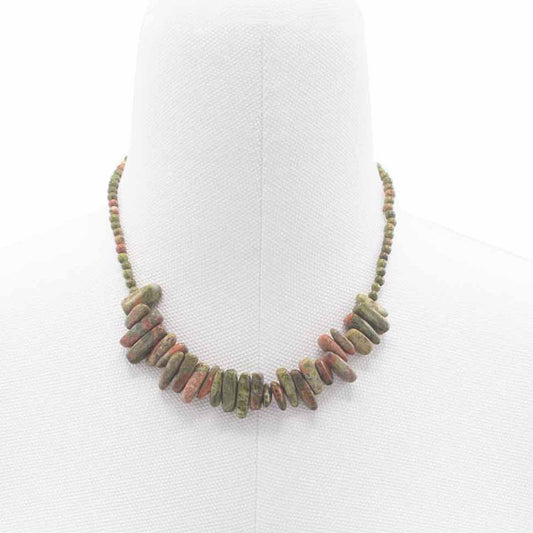 Collar corto de piedras naturales alargadas en tonos verdes y rojizos sobre un busto expositor blanco.