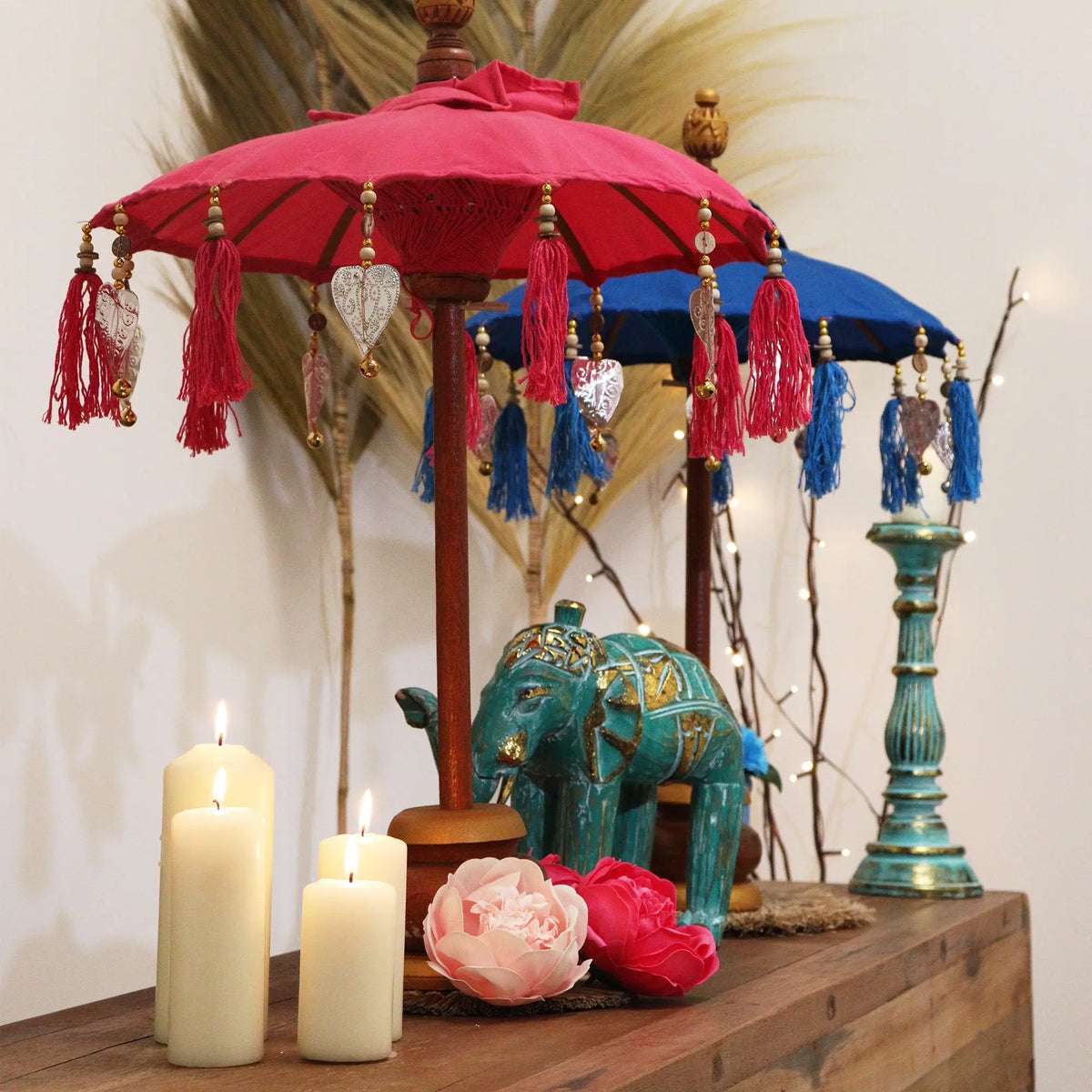 Sombrilla artesanal de algodón fucsia con borlas y decoraciones metálicas, sobre base de madera, estilo balinés.
