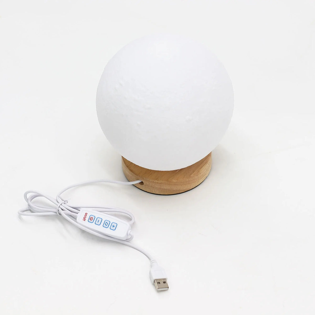 Lámpara esférica tipo luna, blanca con textura, sobre base de madera clara, con cable de alimentación USB y mando.