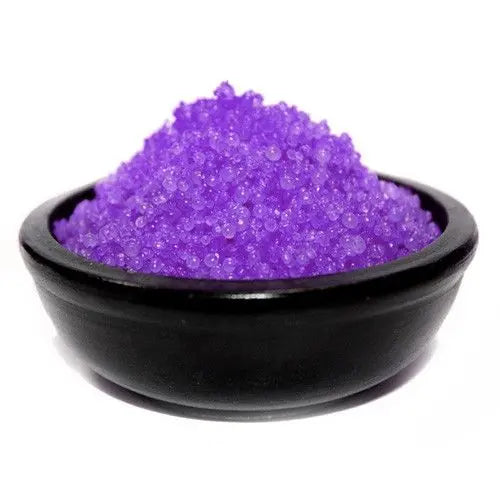 Cuenco negro pequeño lleno de gránulos aromáticos brillantes de color violeta intenso sobre fondo blanco.