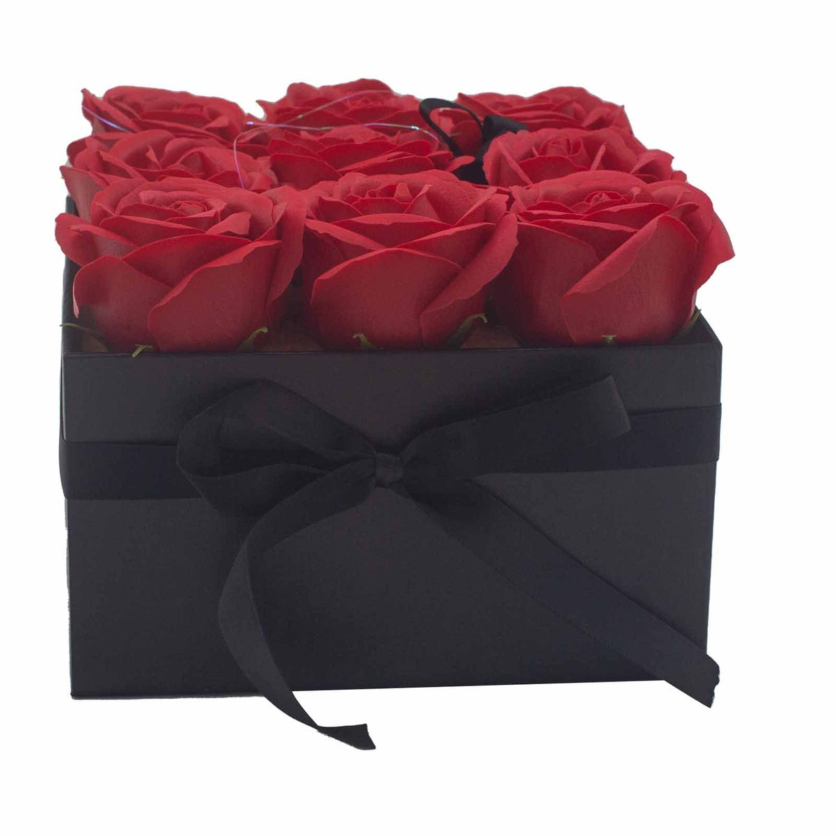 Caja cuadrada negra con lazo, conteniendo 9 rosas rojas de jabón dispuestas en tres filas. Fondo blanco.