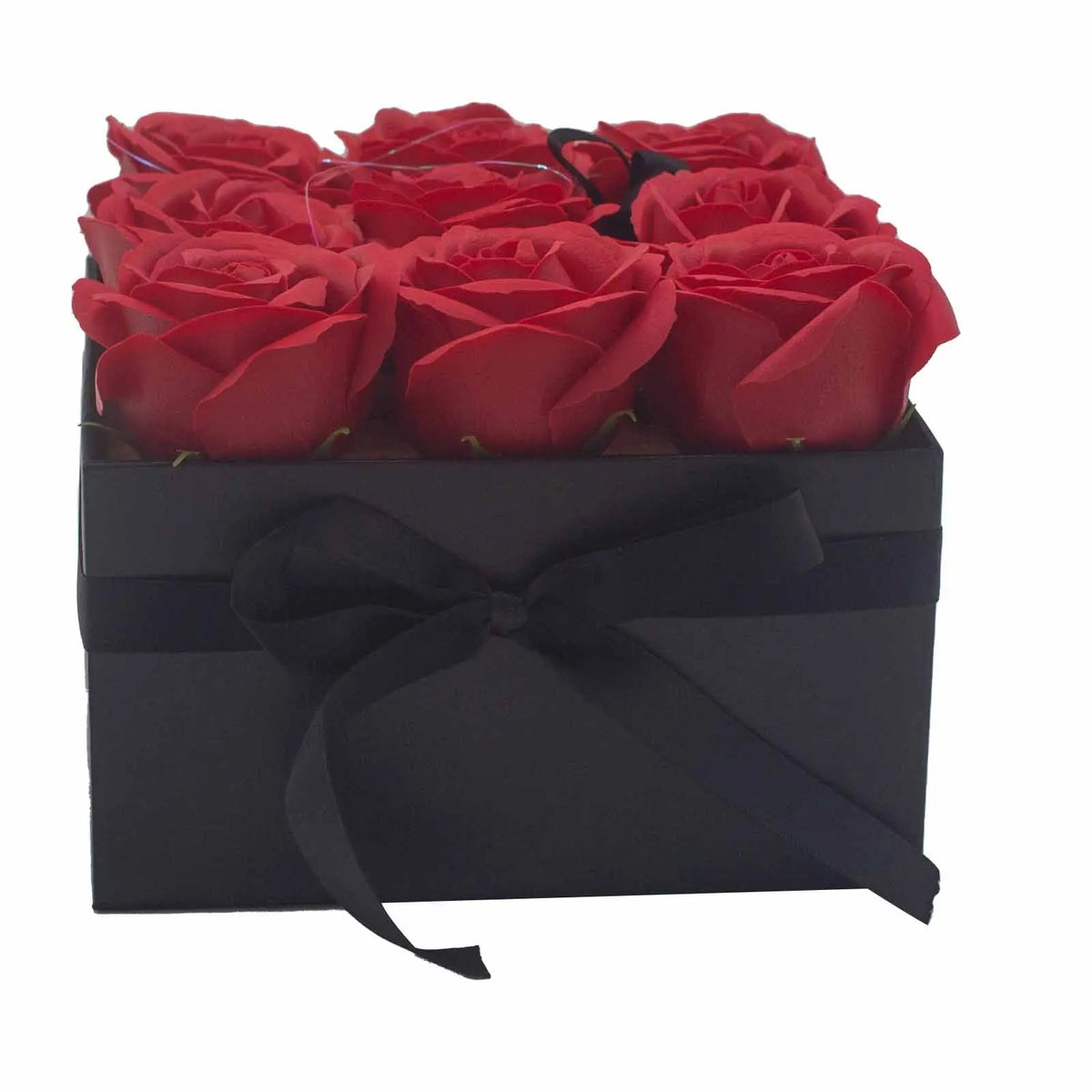 Caja cuadrada negra con lazo, conteniendo 9 rosas rojas de jabón dispuestas en tres filas. Fondo blanco.