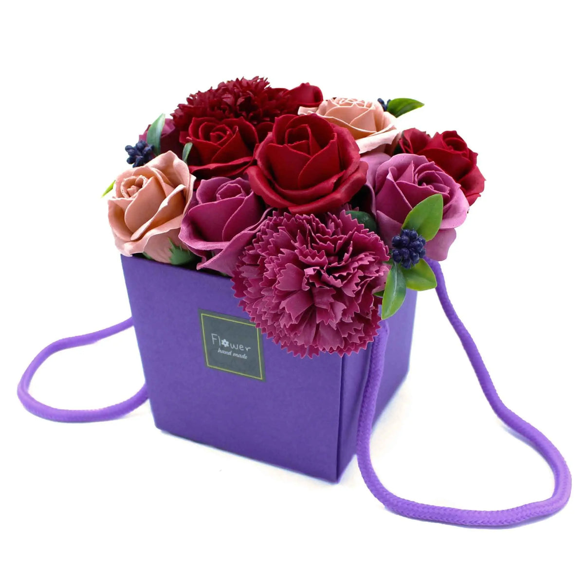Bouquet de rosas y claveles de jabón en tonos rojos y rosas, presentado en una caja cuadrada púrpura con asas de cuerda.