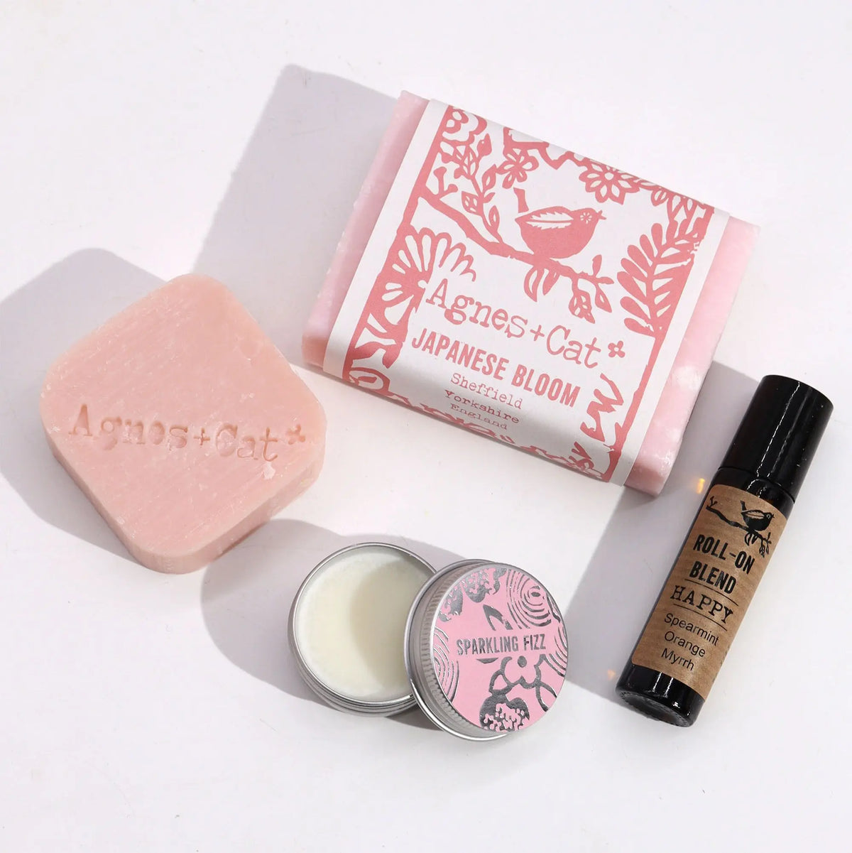 Set de regalo Agnes & Cat: jabón rosa, bálsamo en lata "Sparkling Fizz" y aceite esencial roll-on en frasco oscuro.