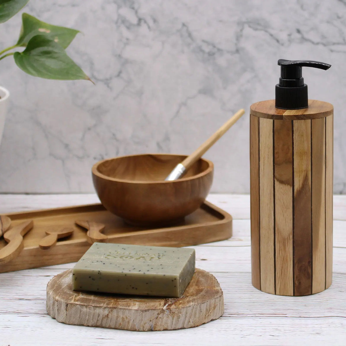 Dispensador de jabón cilíndrico de madera de teca natural con dosificador negro, sobre mesa de madera.