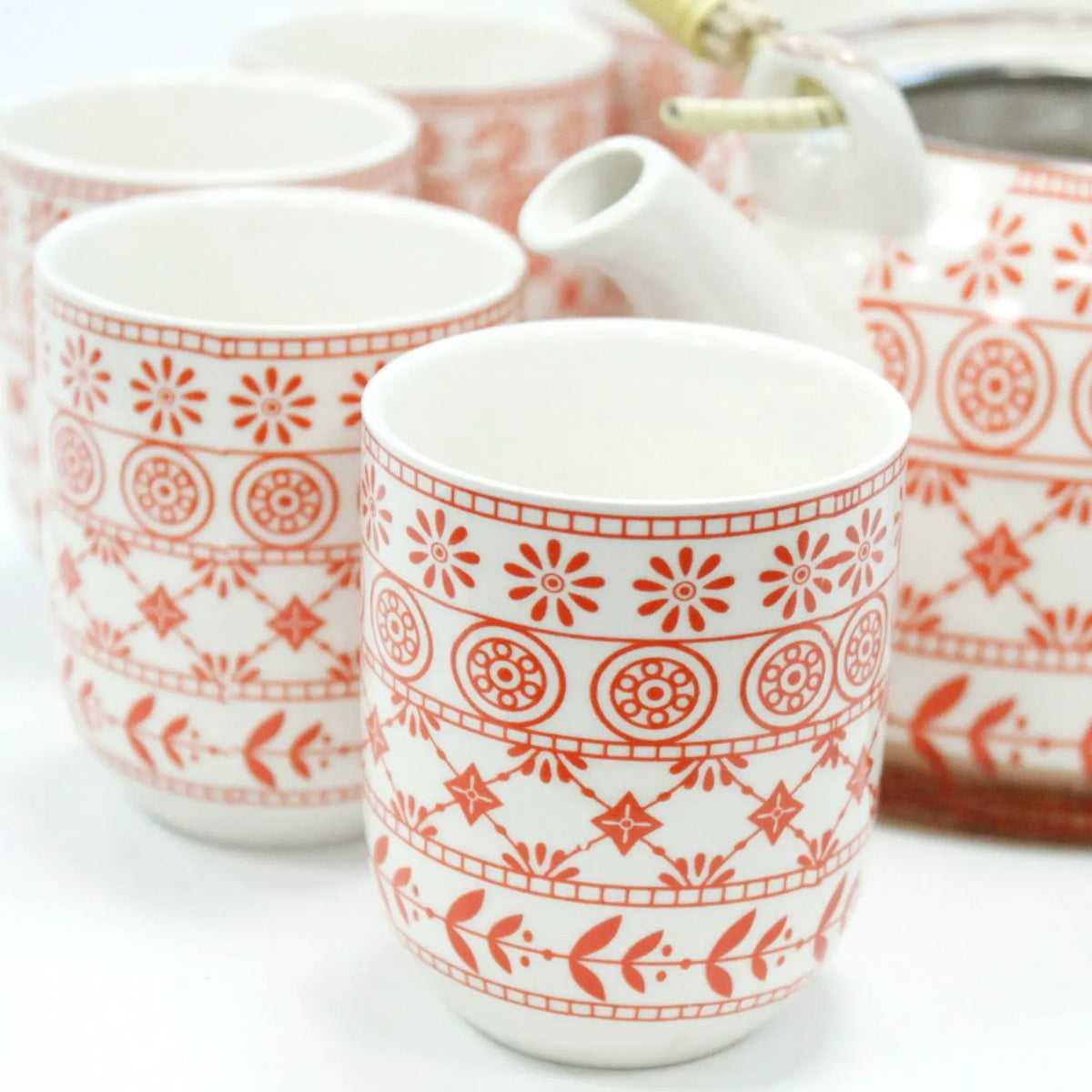 Set de cerámica blanca con tetera y tazas decoradas con patrones geométricos y florales en color naranja.