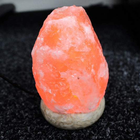 Lámpara de sal del Himalaya con forma irregular y luz naranja cálida, sobre una base de piedra circular.