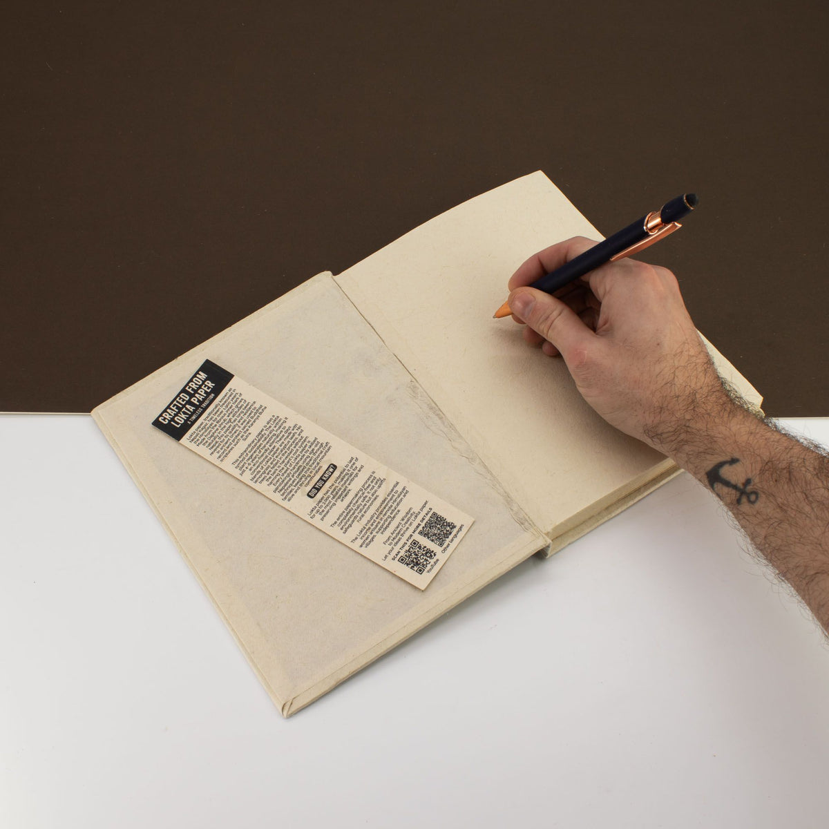Cuaderno abierto color beige con papel en blanco, lapicero azul y marcador de papel kraft, estilo minimalista.