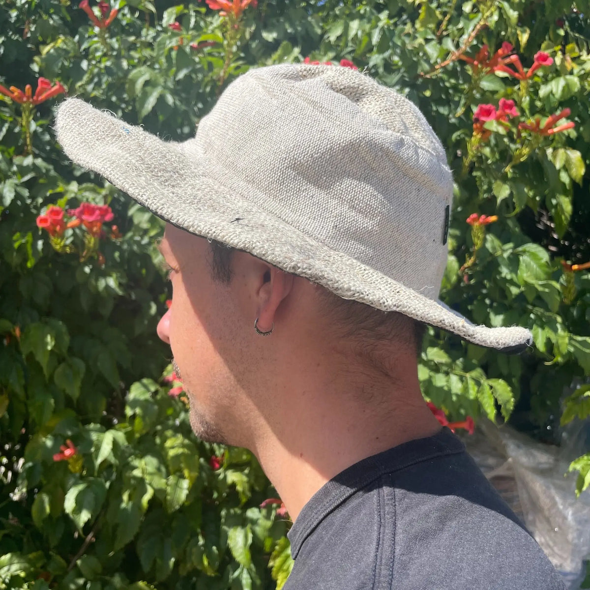 Sombrero boho de cáñamo y algodón color natural, estilo tipo pescador, sobre persona frente a fondo de arbustos verdes.