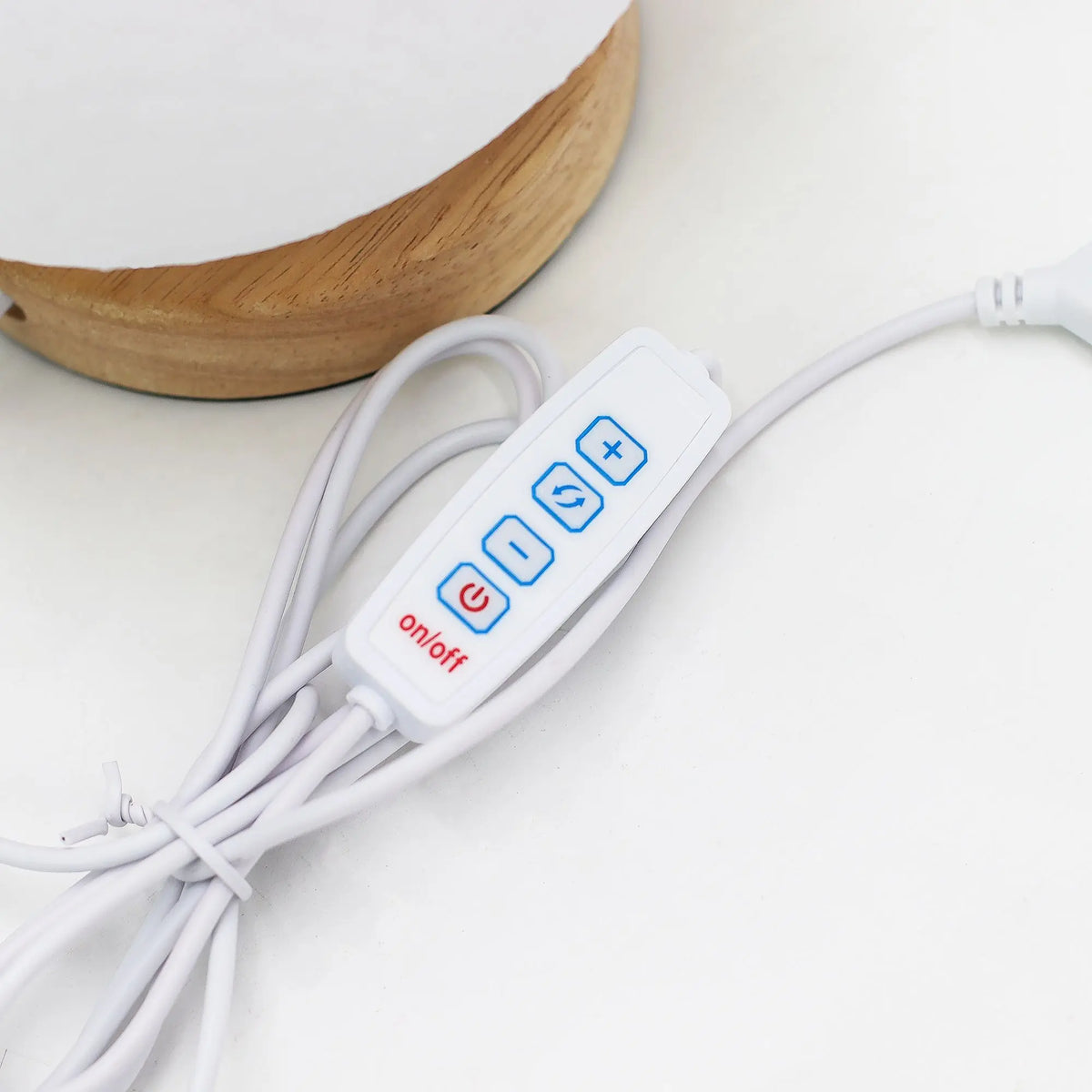 Mando de control USB blanco para lámpara, con botones de encendido, ajuste y cambio de modo, junto a base de madera.