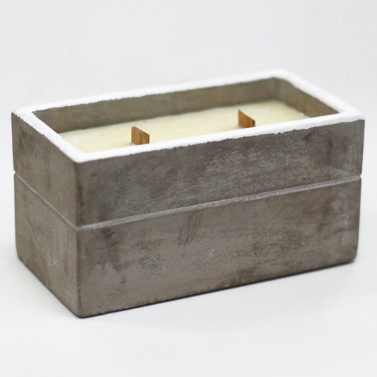 Vela rectangular de hormigón gris con borde blanco, dos mechas de madera y cera crema sobre fondo blanco