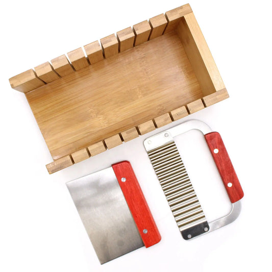 Caja de madera para cortar jabón con guía de ranuras, acompañada de un cuchillo recto y uno ondulado con mango rojo.