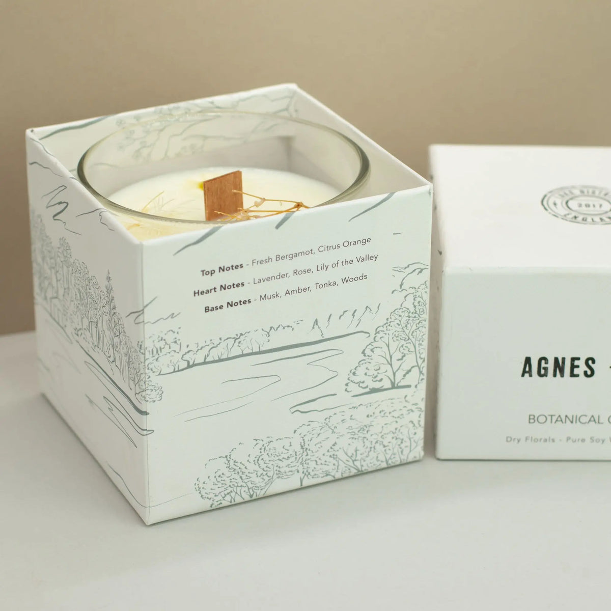 Vela de soya blanca con fragancias florales, en caja blanca decorada con ilustraciones naturales.