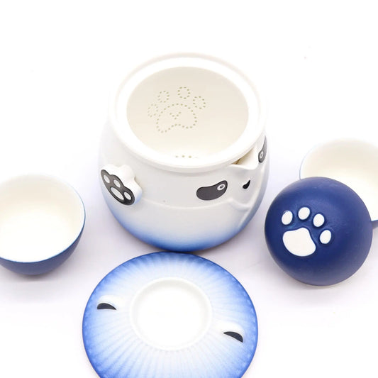 Juego de té cerámico azul y blanco con diseño de panda, incluye tetera con filtro de huella y tres tazas pequeñas.