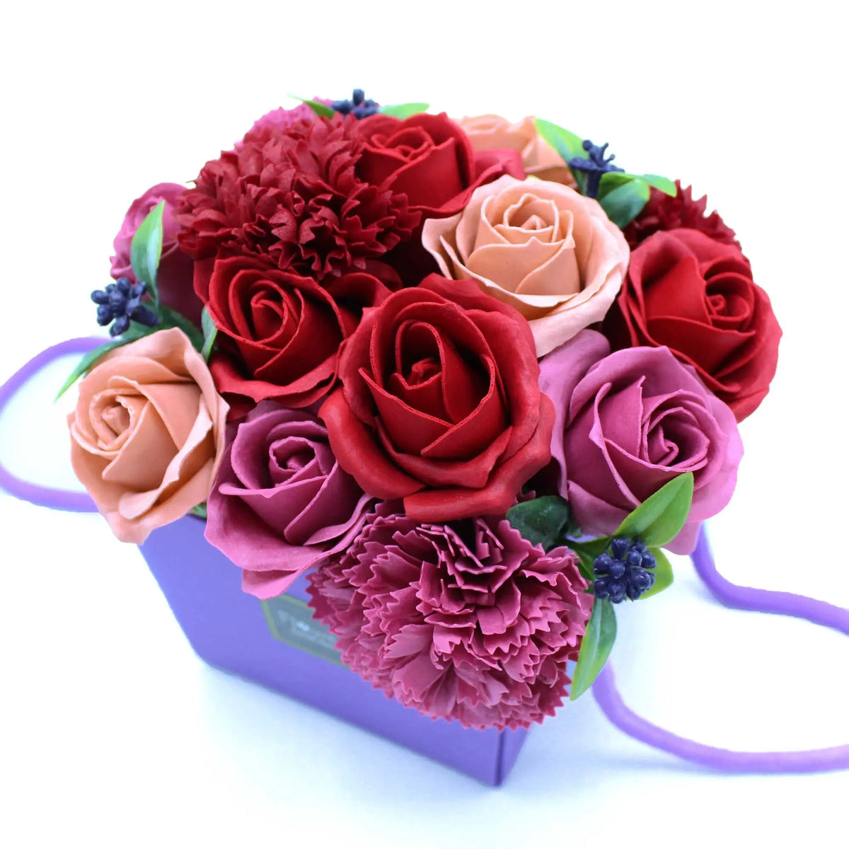 Bouquet de rosas y claveles de jabón en tonos rojos, rosas y beige, en una caja decorativa morada sobre fondo blanco.