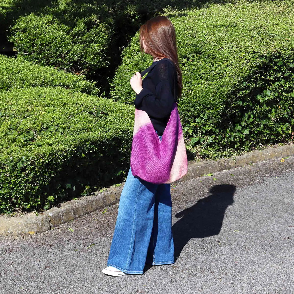 Bolso de hombro de tela suave en degradado fucsia, estilo vintage, colgado al hombro por una joven en un parque.