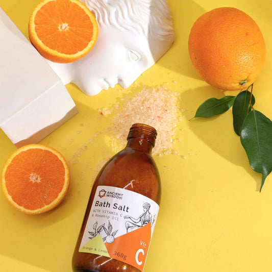 Sal de baño Ancient Wisdom con Vitamina C, naranjas y escultura sobre fondo amarillo brillante. Estilo artístico.