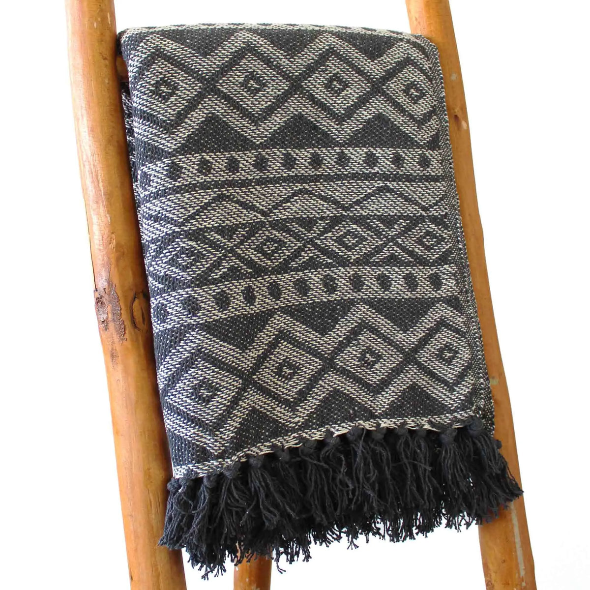 Manta tejida en negro y gris con diseño de diamantes y flecos, ideal para decoración bohemia.