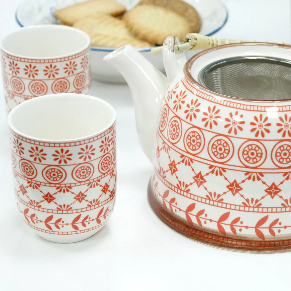 Juego de tetera y tazas de cerámica blanca con patrones geométricos y florales en color naranja, incluye colador.