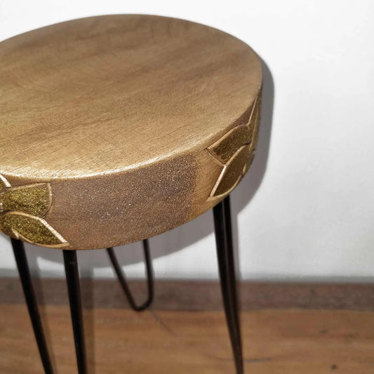 Soporte circular de madera de Albasia con detalles tallados en dorado y patas delgadas de metal negro.
