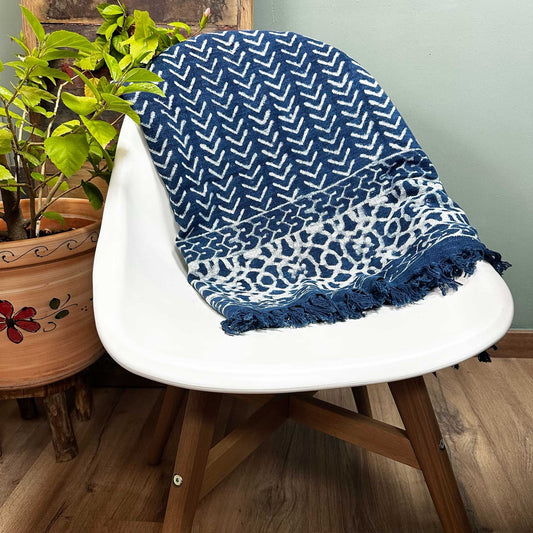 Manta azul marino con patrón geométrico blanco y flecos, ideal para decorar y abrigar.