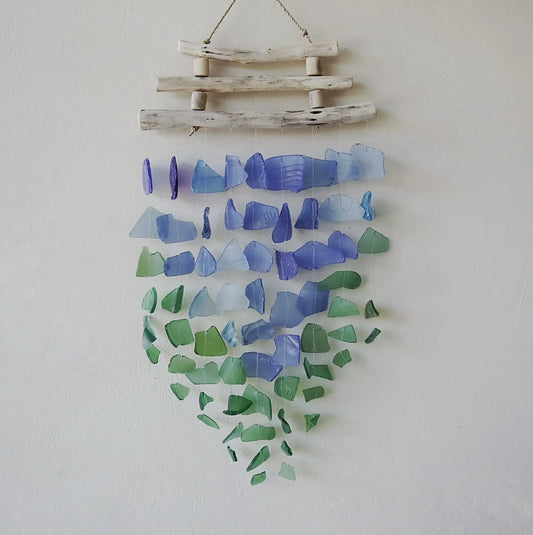 Carillón de piezas de vidrio reciclado en tonos azules y verdes, suspendidas de tres listones de madera clara.