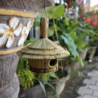 Casa para pájaros redonda de fibra natural, estilo artesanal, colgante, con techo cónico y entrada circular.