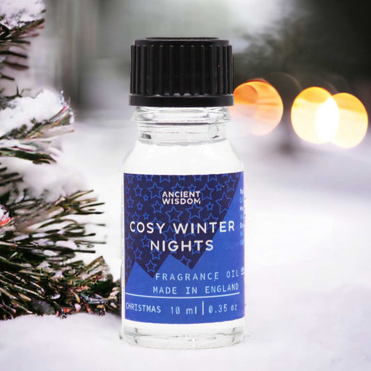 Frasco de vidrio de 10ml con etiqueta azul de estrellas sobre nieve, junto a un árbol de Navidad con luces desenfocadas.