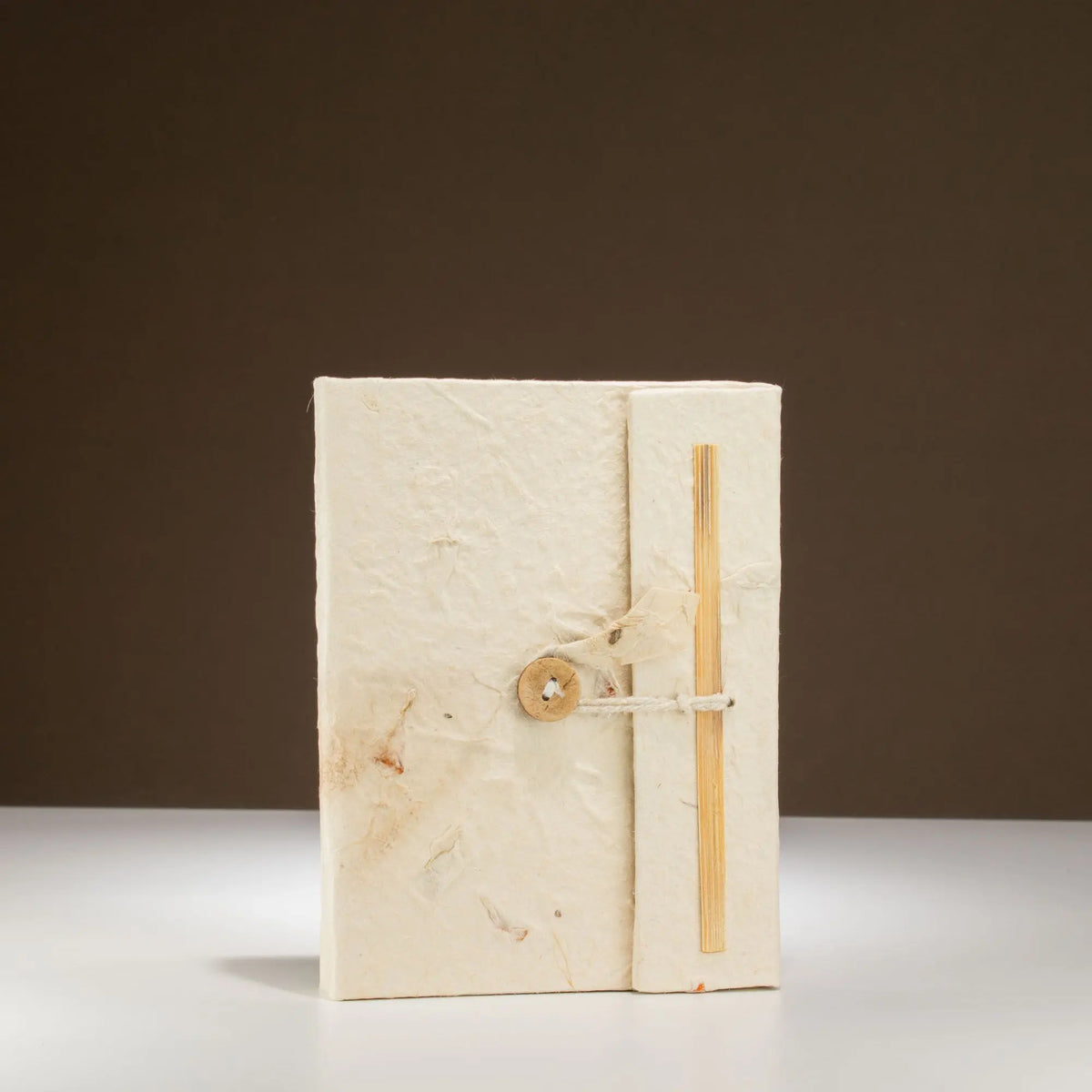 Cuaderno artesanal de papel reciclado blanco con cierre de madera y cuerda, estilo rústico y ecológico.