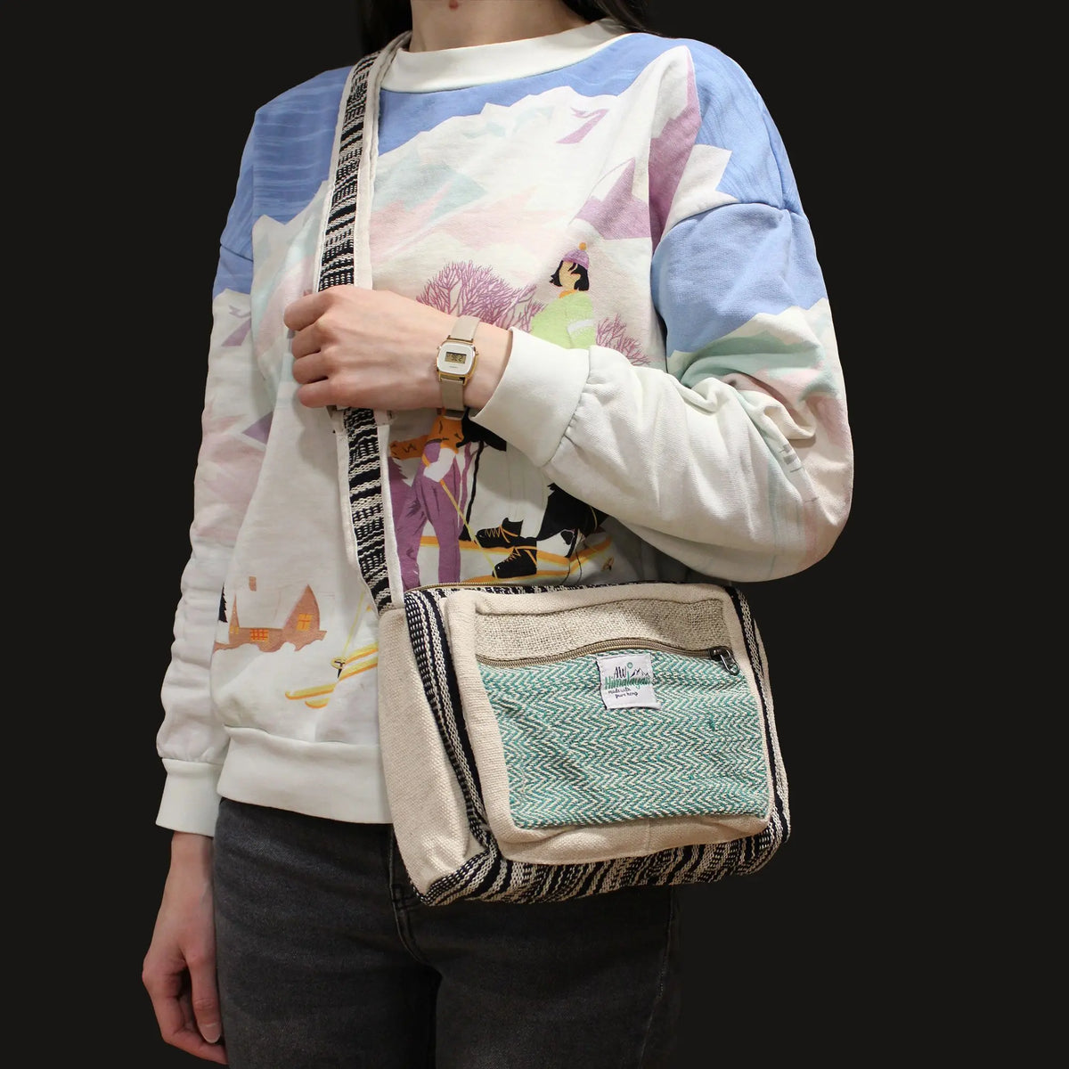 Bolso messenger de cáñamo beige con bolsillo frontal verde y correa tejida con patrones geométricos en blanco y negro.