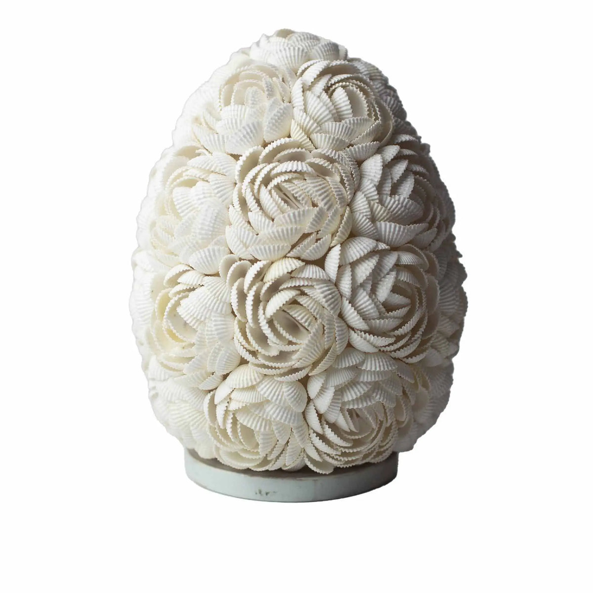 Lámpara ovalada estilo boho hecha de pequeñas conchas blancas dispuestas en forma de flores sobre una base circular.