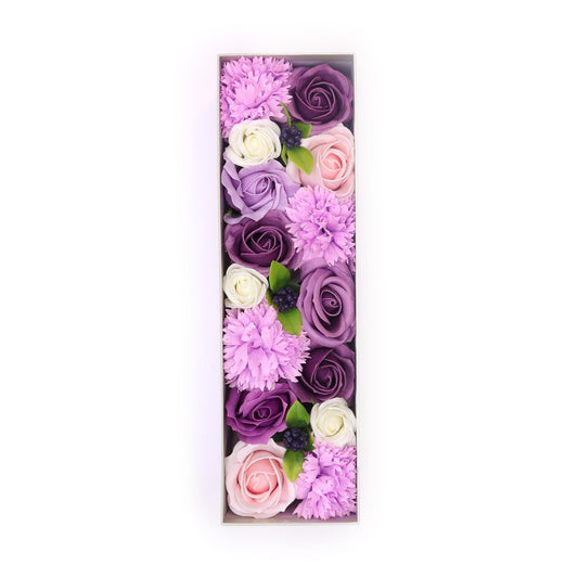 Caja rectangular con rosas y claveles de jabón en tonos lavanda, violeta, rosa y blanco con hojas verdes decorativas.