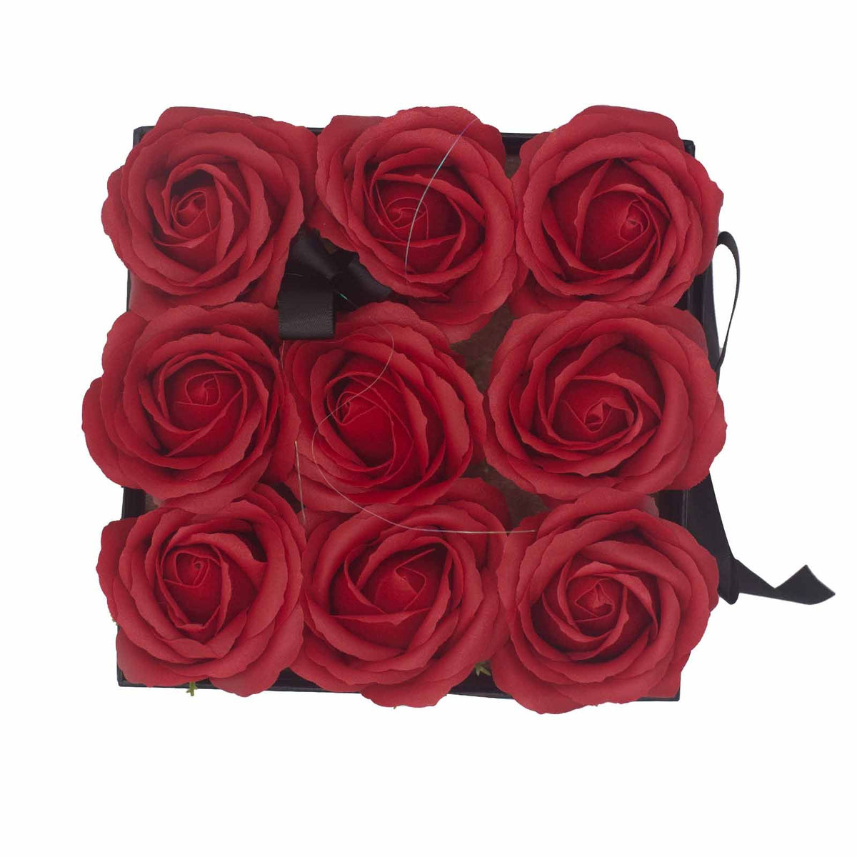 Caja cuadrada negra con 9 rosas rojas de jabón dispuestas en cuadrícula, vista desde arriba sobre fondo blanco.