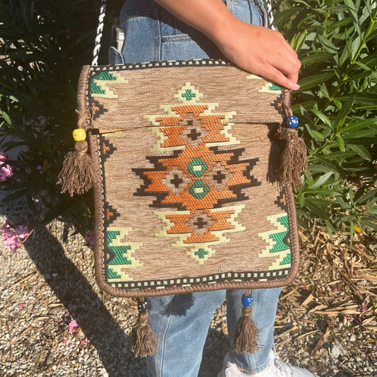 Bolso bandolera de tela tipo kilim beige con diseño geométrico, borlas y cuentas de colores, estilo artesanal.