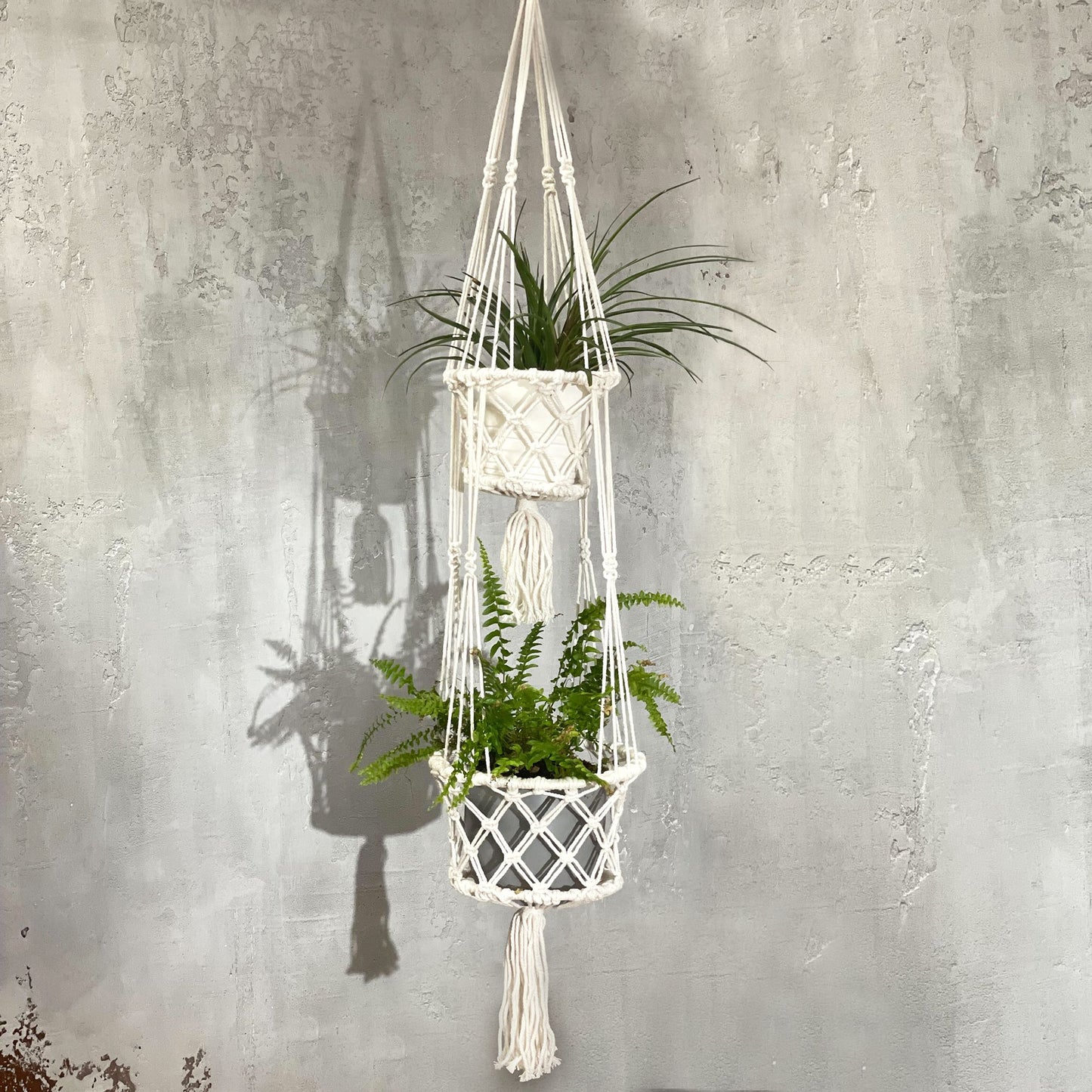 Macramé colgante blanco con dos maceteros y plantas verdes. Ideal para decoración bohemia y natural.