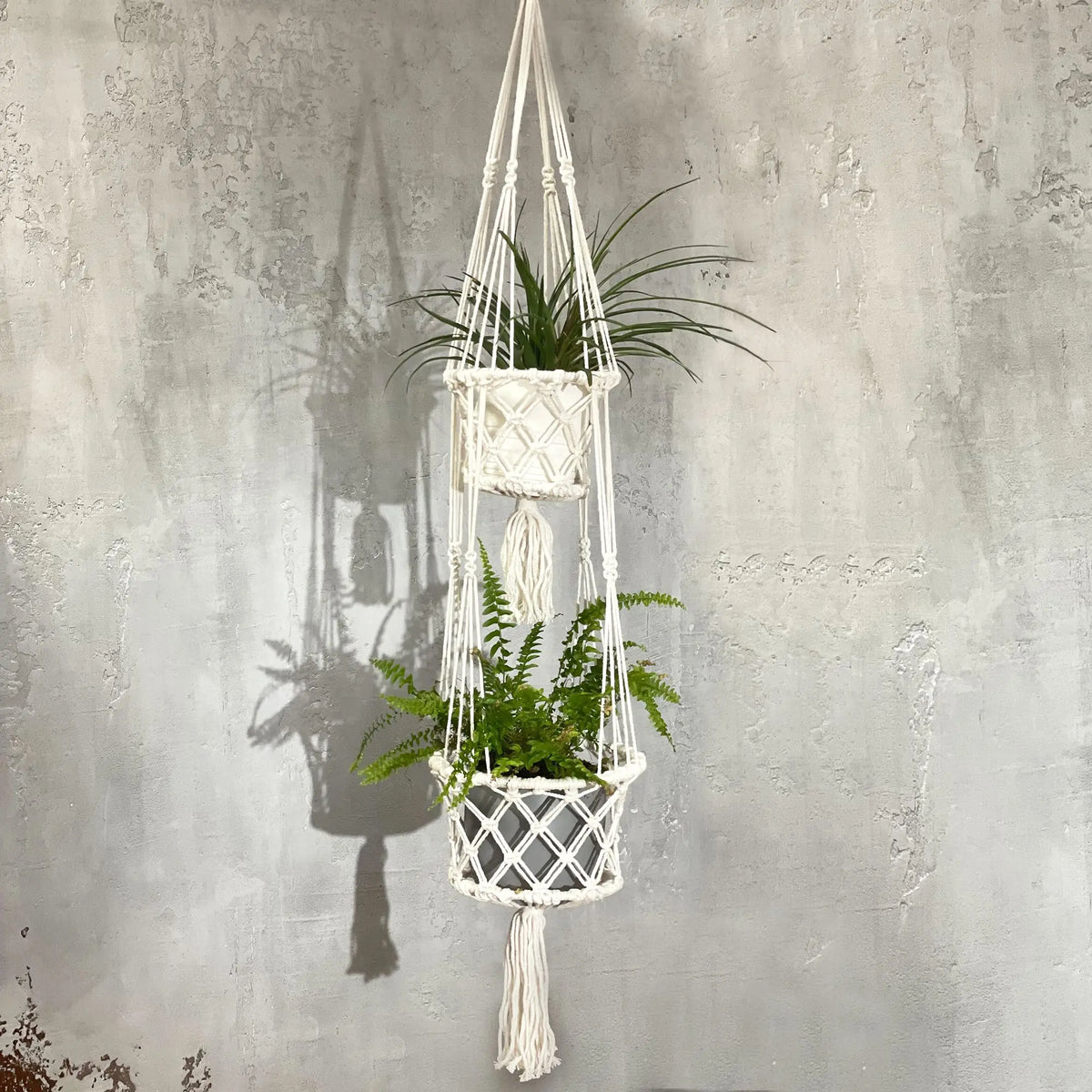 Macramé colgante blanco con dos maceteros y plantas verdes. Ideal para decoración bohemia y natural.