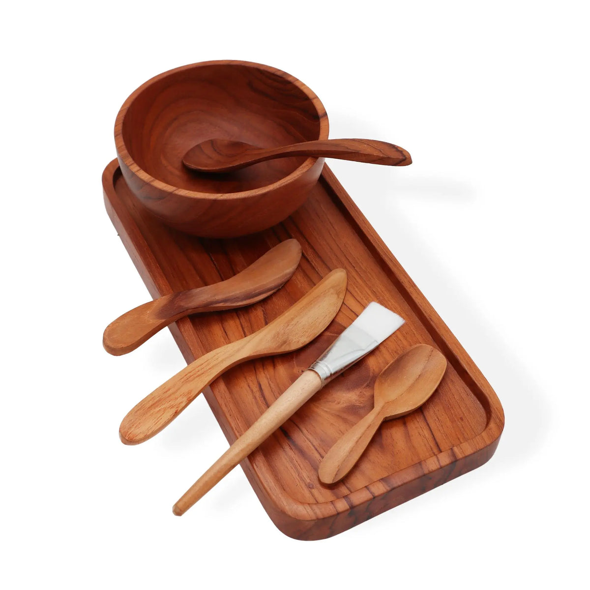 Set de spa artesanal en madera de teca: bandeja, cuenco, espátulas y brocha sobre fondo blanco.