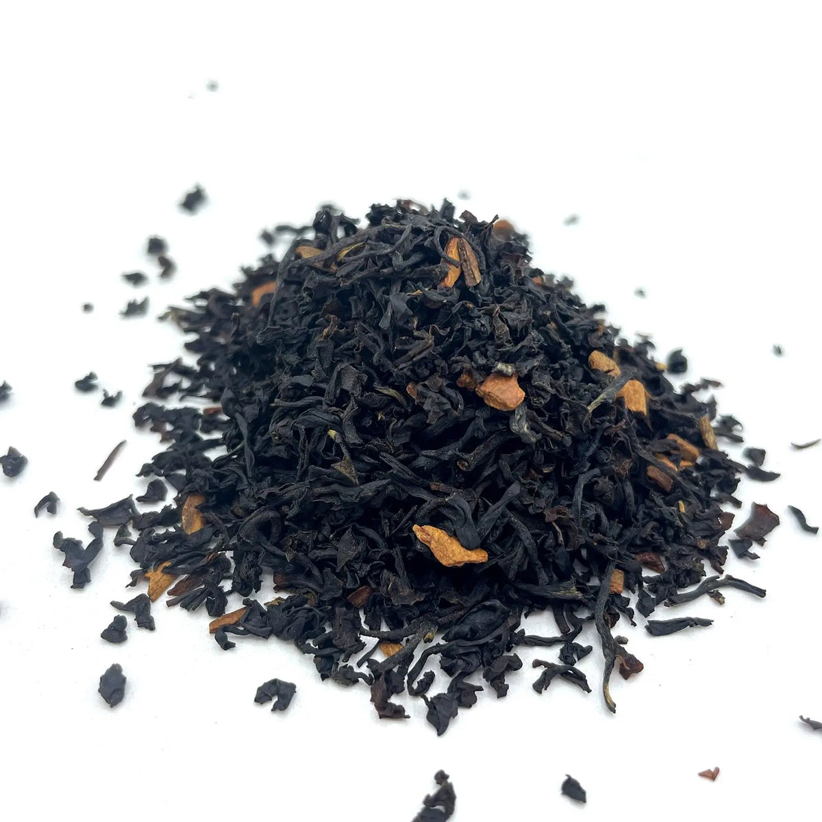 Montículo de hojas de té negro oscuro mezcladas con trozos de cáscara de naranja sobre fondo blanco.