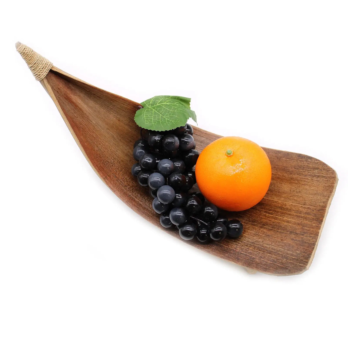 Frutero alargado de hoja de coco natural con uvas y una naranja sobre fondo blanco. Estilo rústico y artesanal.