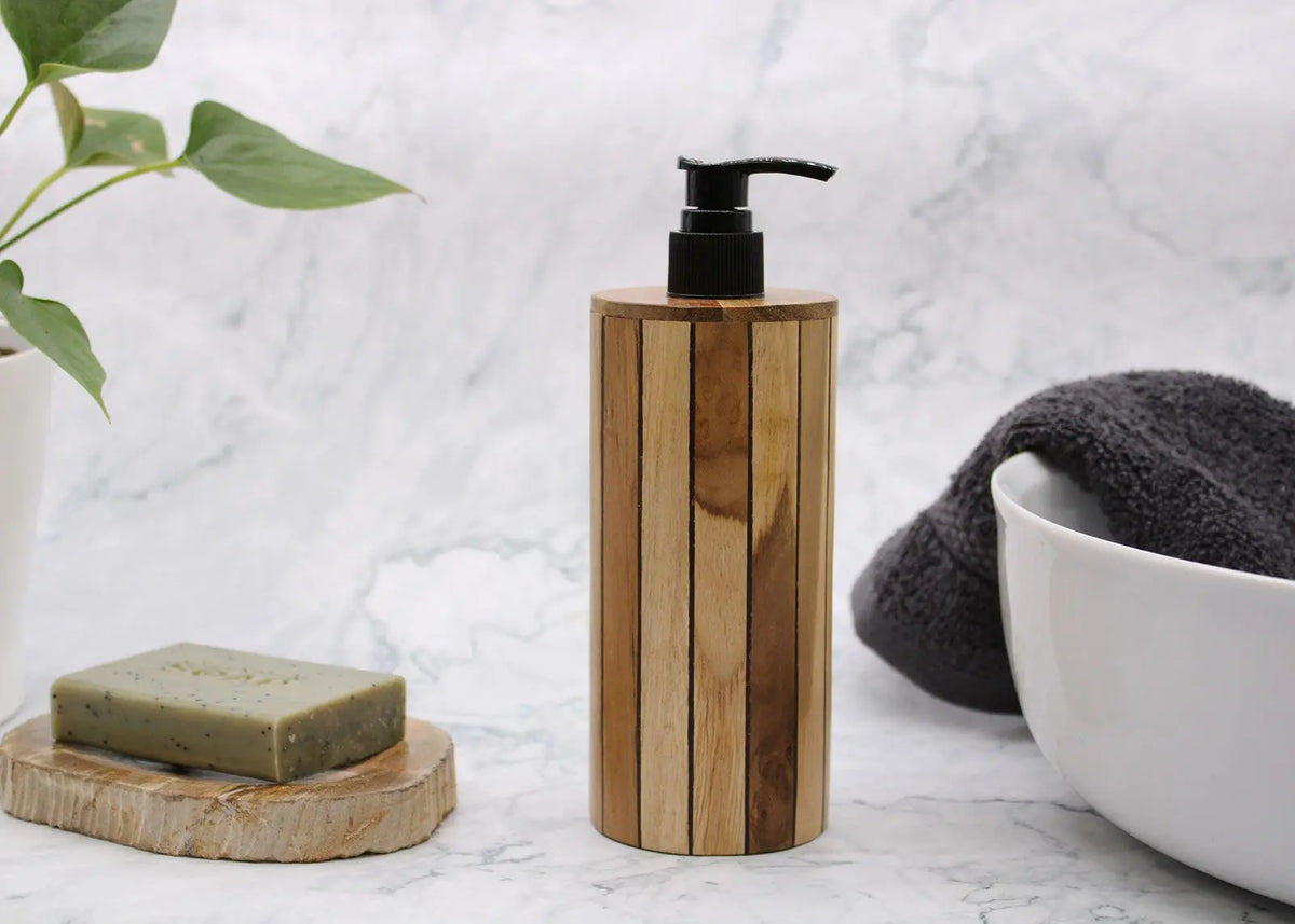 Dispensador de jabón cilíndrico de madera natural con vetas verticales y dosificador de bomba negro sobre fondo mármol.