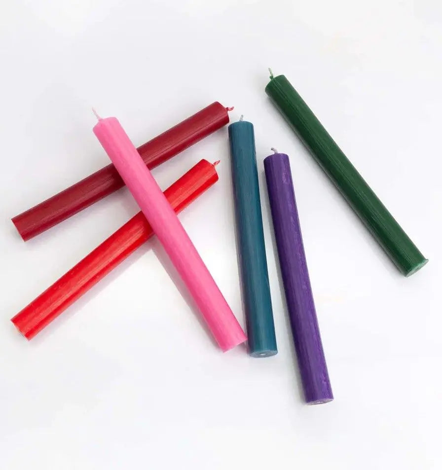Seis velas cónicas de colores surtidos (rojo, rosa, burdeos, azul, morado y verde) sobre fondo blanco.